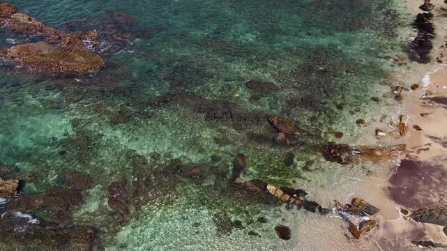 Aerial view of coastal rocks and clear sea water with a glimpse of the sandy shore. Mirissa, Sri Lanka