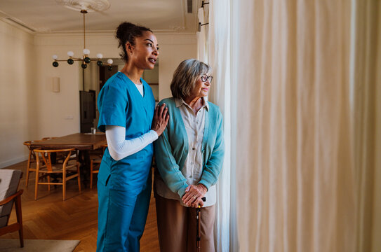 Caregiver in blue scrubs supporting senior woman at home