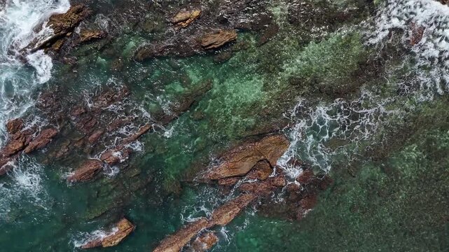 Drone shot of the rocky shoreline with transparent sea water and waves. Mirissa, Sri Lanka