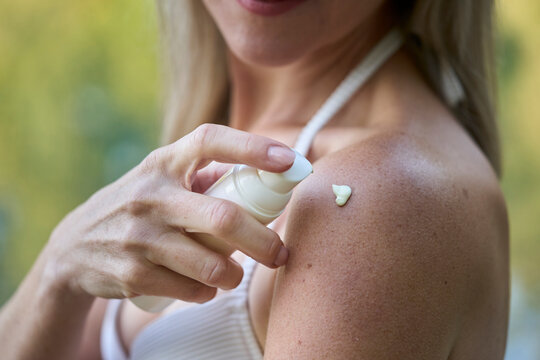 Woman applying sunscreen lotion on shoulder outdoors in summer
