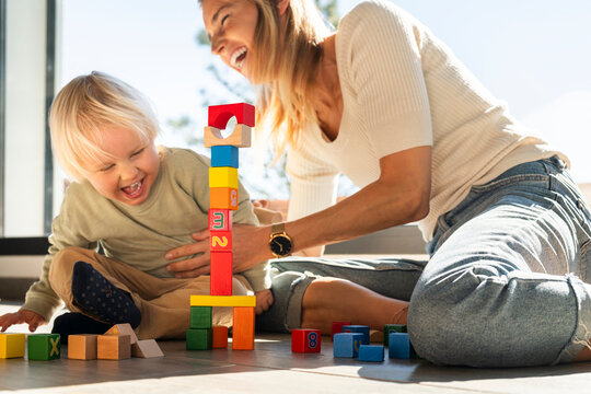 Cheerful mother and son having fun playing with building bricks at home