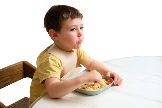 Little boy eating pasta with fork sitting at table. Child with silicone bib having lunch isolated on transparent background. Healthy toddler nutrition and self-feeding development concept.