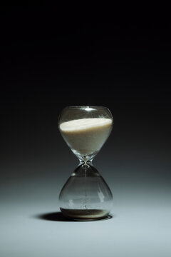 Hourglass measuring time with falling sand on grey studio background
