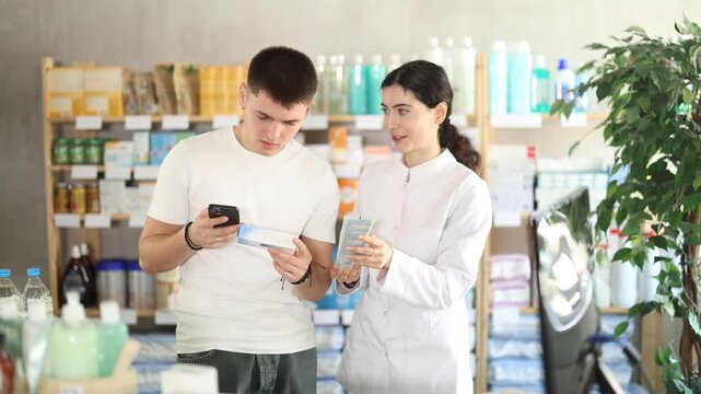  Young man buyer scanning qr code for ointment with young woman pharmacist in pharmacy