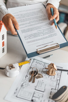 Professional female realtor explains housing terms client while preparing contract in bright office. Real estate transaction with apartment plans, model house and trusted mortgage assistance concept.