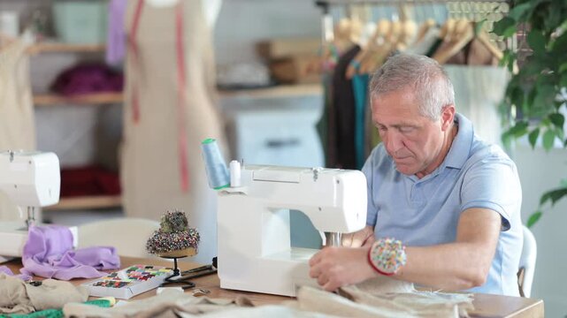 Mature man works as a tailor in a sewing workshop. Production of clothes according to individual measurements. Man sews a sample of clothes