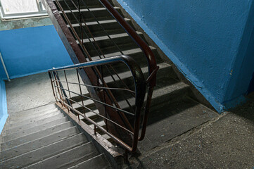 worn concrete staircase with metal railings ascends alongside a blue-painted wall  a window at the top lets in natural light, revealing signs of age and use © evgeniykleymenov