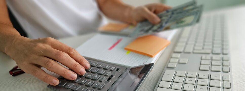 Woman hands holding dollar bills earned by working from computer laptop at home on Internet