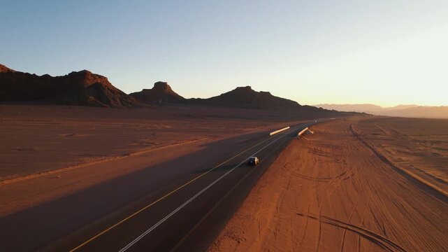 Car driving along a desert road in AlUla, Saudi Arabia on sunset, with red sand and mountains at sunset, capturing a scenic travel route and tourism destination in the Arabian Peninsula. Aerial view