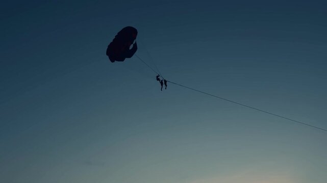 Person parasailing in the sky at sunset over Patong Beach, Phuket, Thailand. High altitude water sport activity and extreme summer fun. Silhouette against a colorful evening sky.Thrilling parasailing 