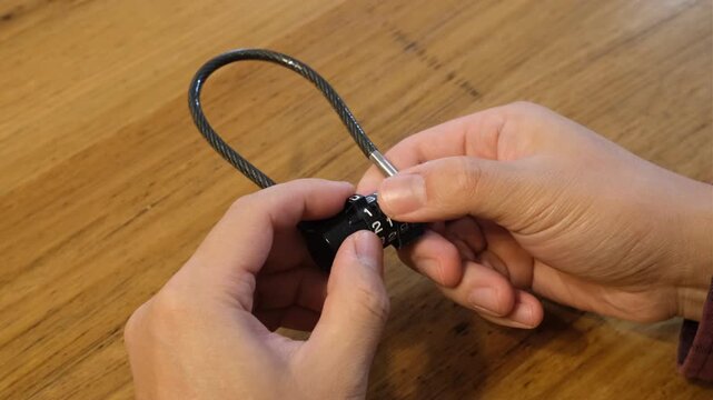 a person's hands holding a combination cable padlock, turning the numbered dials to set or change the security code. Personal security, password, access control and safeguarding valuables