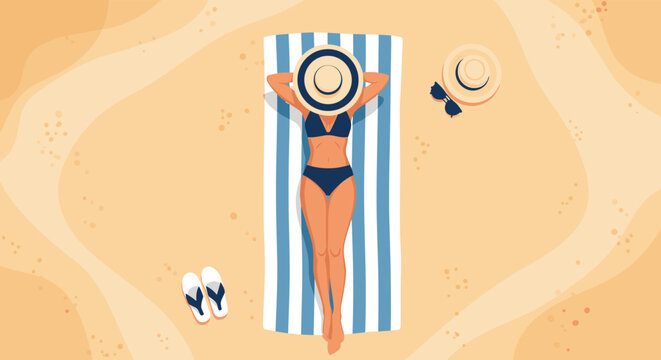 Overhead view of a woman in a dark bikini sunbathing on a blue striped towel with a hat and accessories on a sandy beach.
