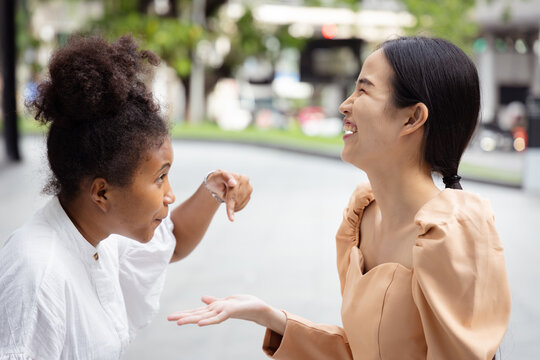 Young African woman telling a joke to her friend then her Asian friend laugh out loud