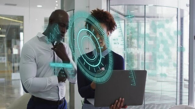 Woman tapping laptop and projecting data charts on glass, man leaning in while analyzing tech data