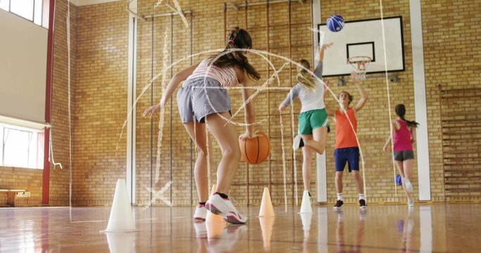 Dribbling teen girl holding orange basketball and navigating cones in school gymnasium, striped top