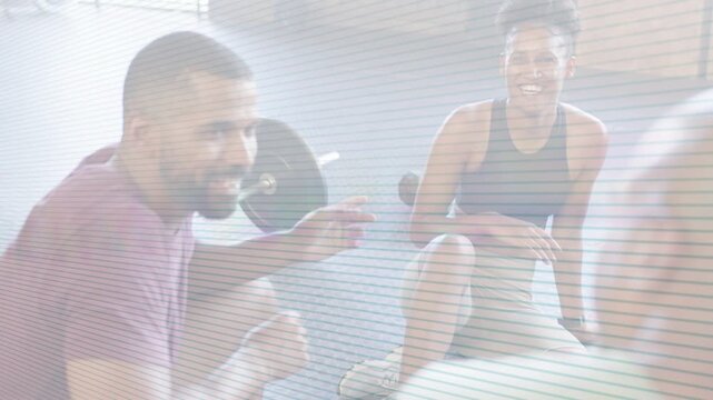 Trainer gesturing and speaking, partner shifting posture and smiling during gym cooldown by barbell