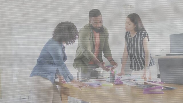 Man presenting sample and initiating team leaning over table, sorting pages, organizing design