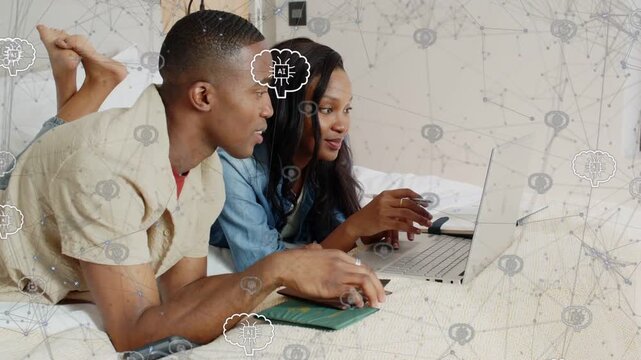 Couple reclining on bed planning trip, right holding card while left viewing passport near laptop