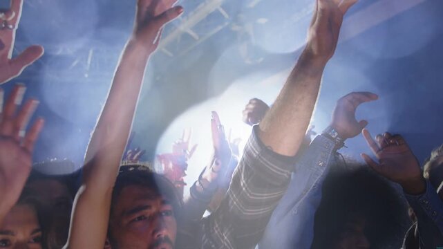 Music crowd raising hands and reacting to spotlight flare intensifying silhouetting truss