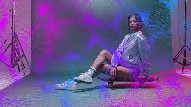 Fashion model posing on red skateboard on light cue for shoot, purple blue waves sweeping backdrop