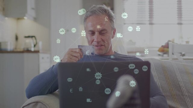 Mature man holding card and typing on laptop, animated payment icons appearing, confirming payment