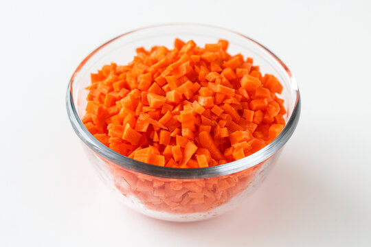 A clear glass bowl of diced or chopped orange carrots, isolated on a white background.