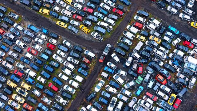 Aerial view of organized rows of cars in a scrapyard. Top down drone shot of various colored damaged cars parked in an industrial auto recycling facility.