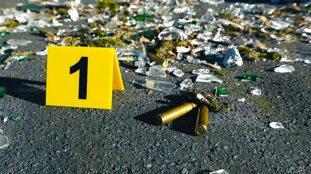 Crime Scene Evidence Marker with Bullet Casings and Shattered Glass on Asphalt