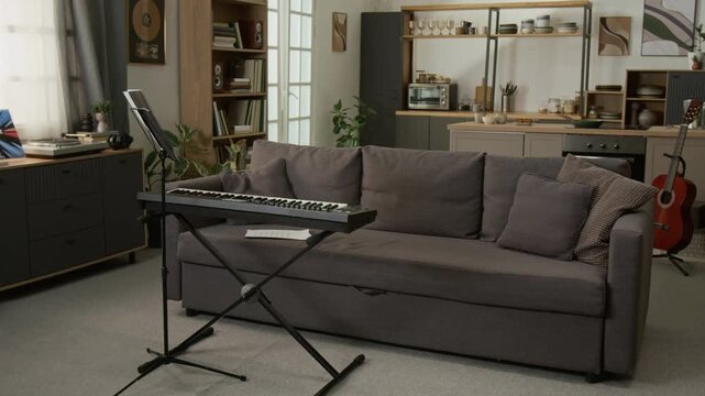 Establishing shot of keyboard and music stand by couch in empty studio apartment interior, no people, copy space Suitable for music school promotions or creative studio advertising