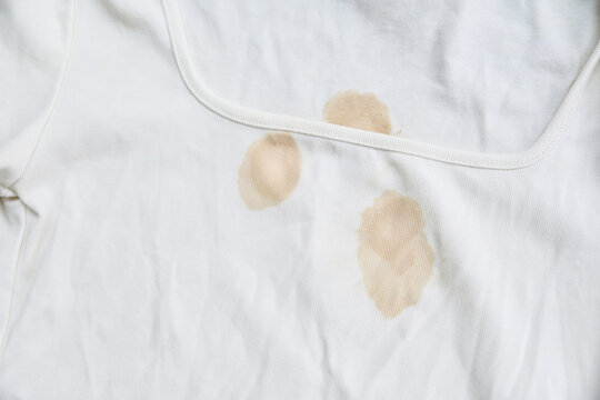 dirty yellow stains on a white rib-knit sleeveless shirt. Dirty clothes concept, sweat or food stains on fabric, laundry problem and stain removal or bleaching service background.