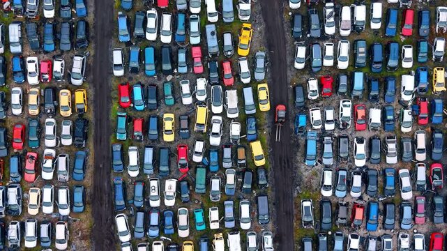 Symmetric overhead view of car scrapyard and dirt paths. Top down perspective of rows of scrapped cars separated by dark dirt tracks in a recycling facility.