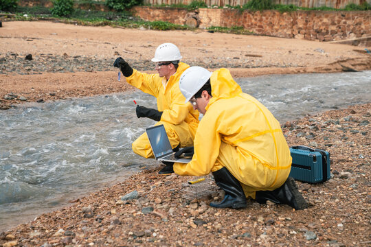Environmental team water testing at industrial river site, workers in protective gear analyzing contamination, ideal for pollution monitoring and safety regulation visuals