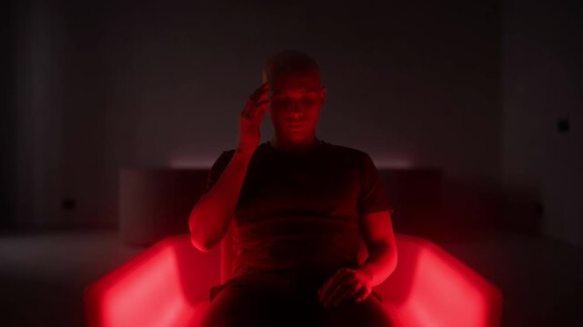 Red Hue Contemplation: In a room bathed in a crimson glow, a pensive individual sits, their expression lost in thought and introspection.
