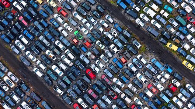 Diagonal aerial view of damaged cars in scrapyard. Factual drone shot of rows of old vehicles at an auto salvage facility for spare parts extraction.