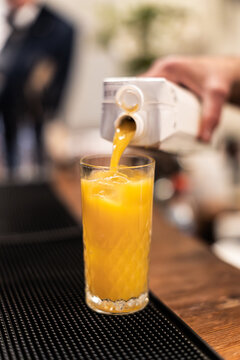 Close-up of orange juice being poured from a carton into a tall ice-filled glass on a bar mat during event drink service