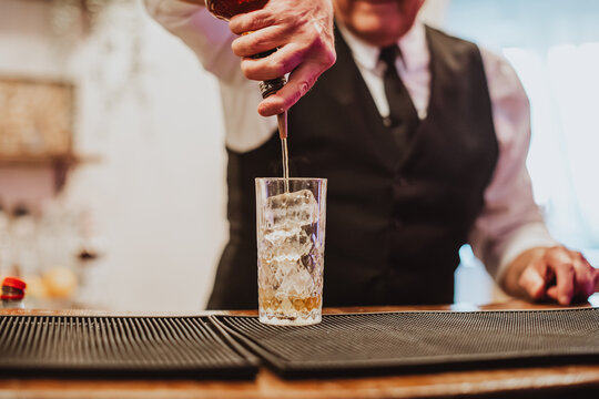 Bartender pours liquor into a tall glass filled with ice on a bar mat, creating a polished event drink service scene