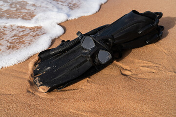 Black snorkeling mask with snorkel and flippers lying on a sandy beach near the sea waves during summer vacation. © Dmitri
