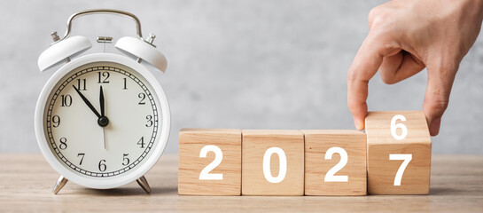 Happy New Year with vintage alarm clock and hand flipping 2026 change to 2027 block. Christmas, New...