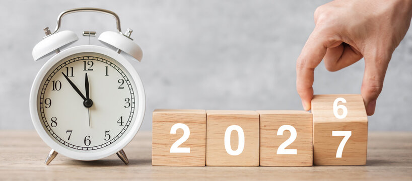 Happy New Year with vintage alarm clock and hand flipping 2026 change to 2027 block. Christmas, New Start, Resolution, countdown, Goals, Plan, Action and Motivation Concept