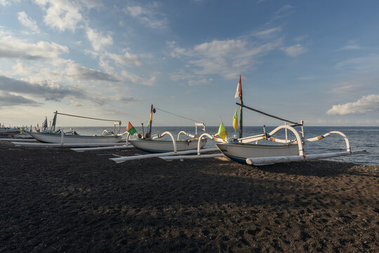 Traditional Balinese fishing boats on a black sand beach in Amed, Bali, with calm sea and late-afternoon light.