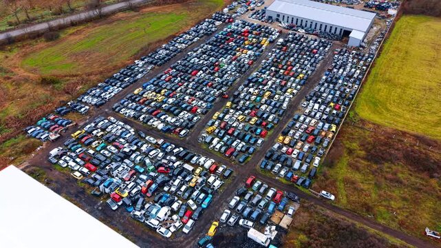Large scale automotive scrap yard facility from drone view. Panoramic aerial shot of an extensive vehicle recycling lot with hundreds of cars and industrial buildings.