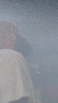 Vertical video: Bearded man with cap at left tilting head reacting to light shifts in haze for film