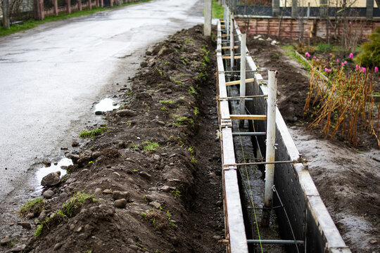 Perspective view down the formwork channel with metal reinforcement near a quiet residential road after rainfall