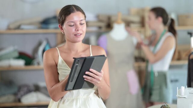 Woman seamstress draws image of future suit in tablet, creates electronic prototype of finished product. Designer use stylus to draw on graphics tablet. Assistant work with mannequin in background