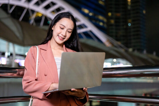 Asian young businesswoman using laptop computer outdoors in the city. 