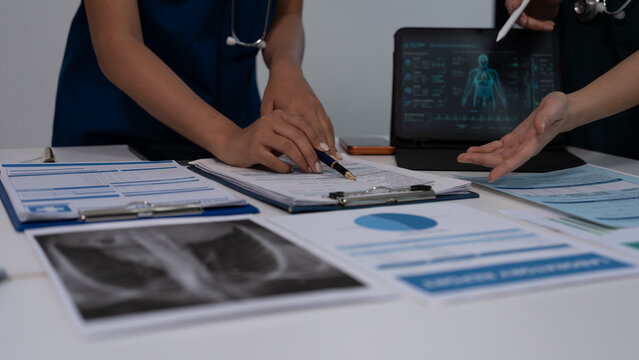 Medical team in scrubs reviewing patient charts and lab reports on desk with laptop showing digital anatomy scan in hospital office.
