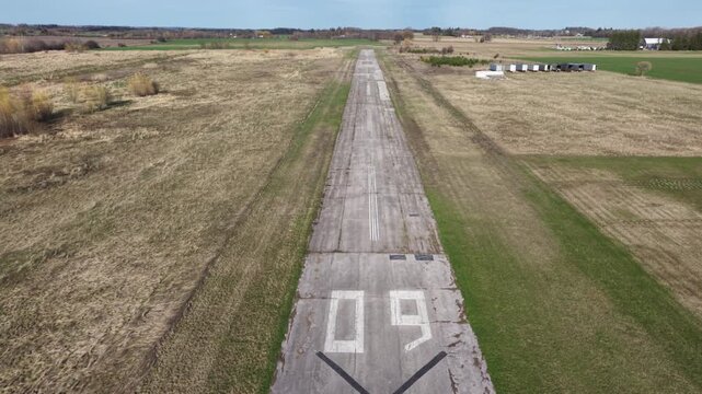 Drone shot flying forward along the weathered asphalt of decommissioned runway 09 at Markham Airport, showing the closure 'X' and rural surroundings