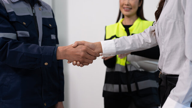 Business handshake between client and engineer, with safety supervisor in reflective vest holding clipboard in background, representing partnership and workplace compliance.