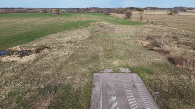 Drone shot pulling back along the weathered asphalt of decommissioned runway 09 at Markham Airport, revealing the closure X and rural fields