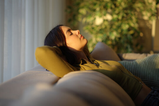 Woman is relaxing at sunset sitting on a sofa at home